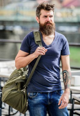 Seyahat ve tatil konsepti. Sakallı ve bıyıklı kaslı adam büyük sportif çanta taşıyor. Turist bagaj ile şehir keşfetmek. Omzunda ağır bir çanta var. Omuzda büyük çanta şeyler taşıyın