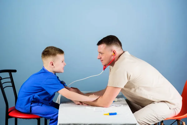 Charla profesional. medicina y salud. Un niño pequeño con papá jugando. Carrera futura. Asistente de laboratorio de enfermería. médico de familia. niño feliz con padre con estetoscopio. padre e hijo en uniforme médico — Foto de Stock