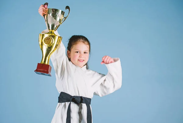 sport success in single combat. practicing Kung Fu. happy childhood. winner little girl in gi sportswear. small girl with champion cup. martial arts. energy and activity for kids. Striking the pose