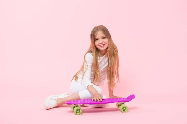 Дівчина розважається з дошкою пенні рожевим фоном. Дитяча чарівна дитина довге волосся обожнює кататися на дошці копійки. Щасливе дитинство. Їздити на дошці пенні і робити трюки. Дівчинка любить кататися на скейтборді. Активний спосіб життя — стокове фото