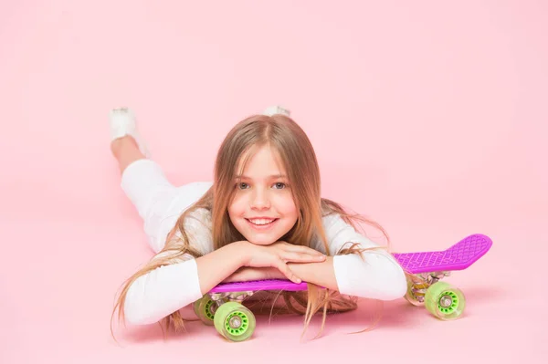 トレンディな女の子。子供愛らしい子供の長い髪はペニーボードに乗って崇拝。ペニーボードに乗って、トリックを行います。女の子はスケートボードに乗るのが好きです。アクティブなライフスタイル。ペニーボードピンクの背景を楽しんでいる女の子 — ストック写真