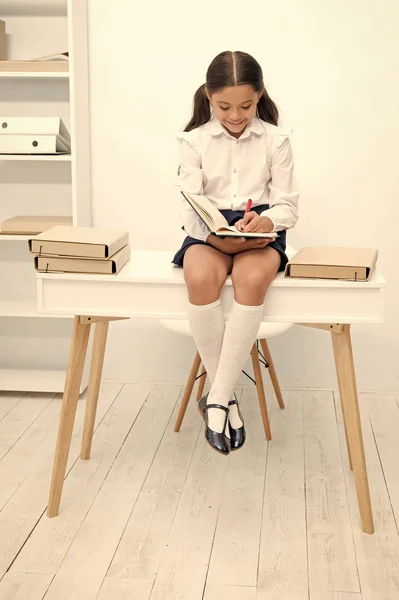 Детская концепция. Ребенок улыбается, записывая в блокнот на столе. Малыш делает уроки. Милый ребенок тщательно делает домашнее задание. Образование имеет предел, но обучение не — стоковое фото
