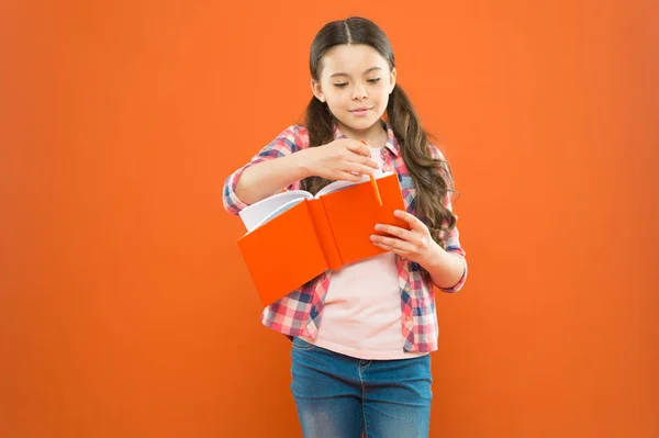 Entrando en un mundo diferente. Educación literaria. Niña con libro de literatura inglesa. Niño pequeño leyendo literatura infantil sobre fondo naranja. Lección de literatura en la escuela — Foto de Stock