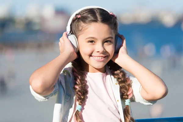 Siguiendo la corriente. Adorable usuario de auriculares. Niño pequeño con auriculares blancos ajustables. Niña usando auriculares inalámbricos bluetooth al aire libre. Lindo niño escuchando música en auriculares estéreo — Foto de Stock