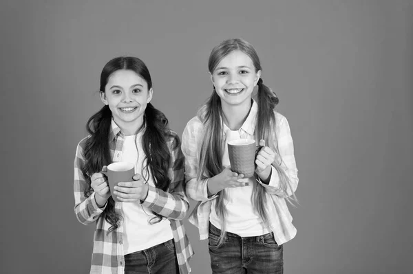 Se till att barnen dricker tillräckligt med vatten. Flickor barn håller koppar orange bakgrund. Systrarna hålla muggar. Dricka te bryter. Koppla av med dryck. Te paus. Barn dricker inte tillräckligt under skoldagen — Stockfoto