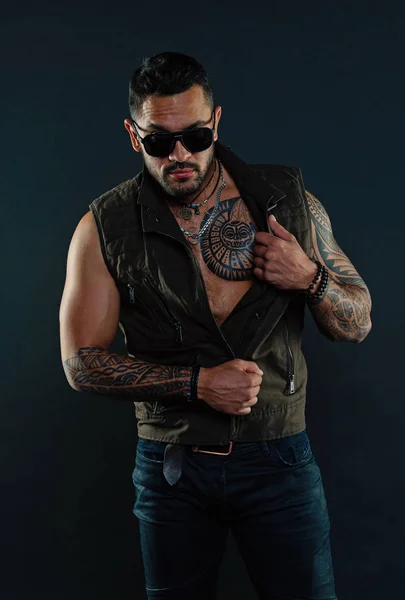Bearded man with tattoo on chest and arms. Fashion style and trend. Tattoo model with beard on unshaven face. Tattooed man with biceps and triceps. Fashion macho in trendy sunglasses