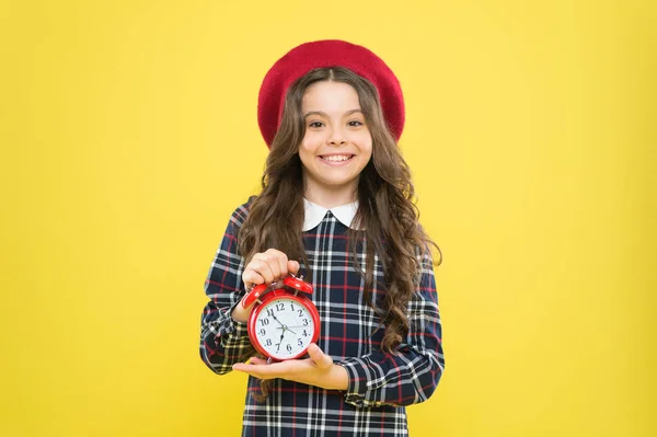 Clock is ticking. Small child smiling with mechanical clock on yellow background. Adorable kid with long brunette hair and wakeup clock. Happy little girl holding alarm clock — Stock Photo, Image