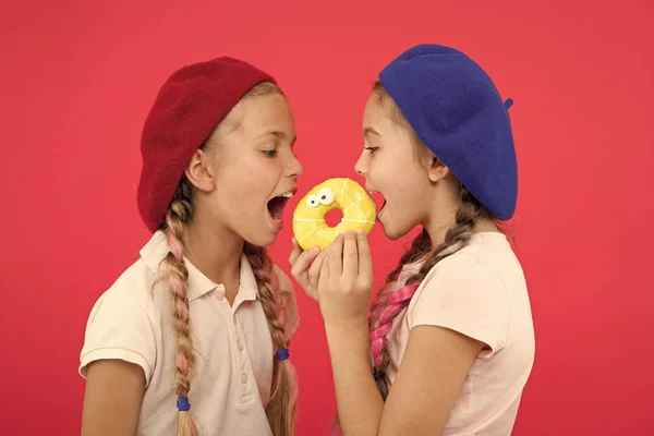 Sweet life. Sweets shop and bakery concept. Kids fans of baked donuts. Share sweet donut. Girls in beret hats hold donut red background. Kids playful girls ready eat donut. Friendship and generosity