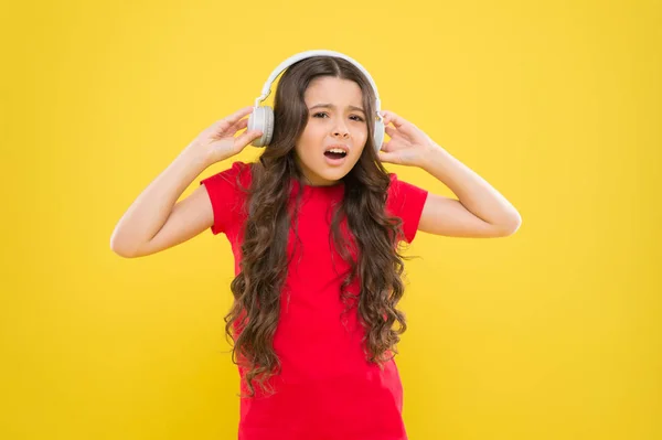 ¿Por qué mis auriculares suenan bajos? Niña usando auriculares sobre fondo amarillo. Lindo niño escuchando música en auriculares estéreo para oídos. Adorable niño pequeño con auriculares modernos — Foto de Stock