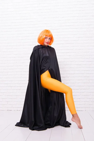 A moda é a vida dela. Modelo de moda vestindo cabelo de peruca laranja e roupão preto na parede de tijolo branco. Menina sexy com aparência de moda. Moda e beleza — Fotografia de Stock