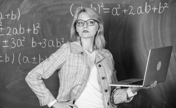 Distance education concept. Woman teacher wear eyeglasses holds laptop surfing internet. School innovation concept. Teacher elegant lady with modern laptop surfing internet chalkboard background