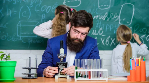 Man bearded teacher work with microscope and test tubes in biology classroom. Explaining biology to children. Biology plays role in understanding of complex forms of life. School teacher of biology