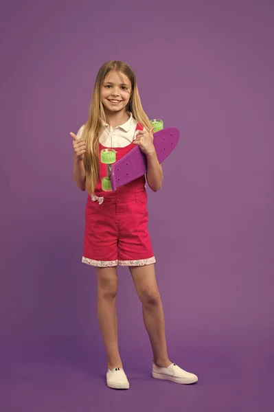 Jeune fille prête à monter penny board. Le passe-temps moderne des jeunes. Panneaux Penny également connu sous le nom de mini croiseur. Fille visage heureux tient penny conseil fond violet. Initialement conçu comme skateboard pour filles — Photo