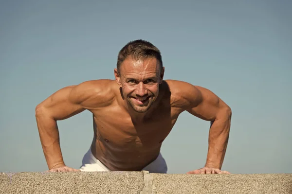 Man doing push ups outdoor blue sky background. Guy motivated workout. Sportsman improves his strength by push up exercise. Push ups challenge. Improve endurance by push ups
