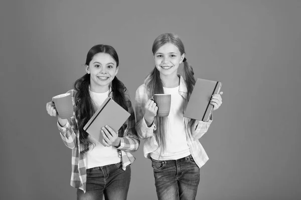 Lectura de actividad agradable. Chicas niños con libros y tazas de té fondo naranja. Los amigos pasan el tiempo libre leyendo libros. Descansando. Beber té mientras lees un libro. Hermanas relajándose con la bebida — Foto de Stock