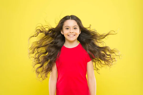 J'ai juste lâché mes cheveux. Enfant heureux avec des cheveux coulants sur fond jaune. Petit enfant avec un sourire mignon et des cheveux ondulés texturés. Adorable petite fille souriant avec de longs cheveux bruns — Photo