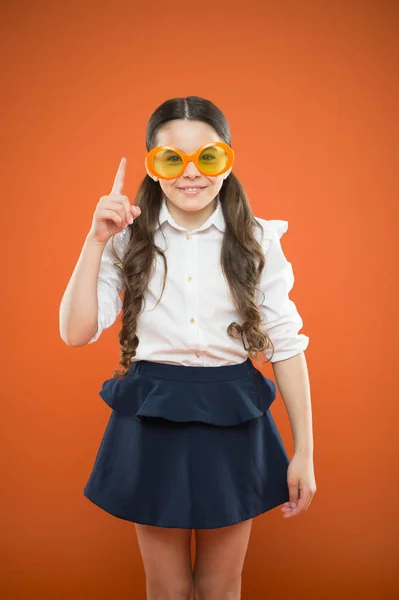 Die beste Brille für ihre Gesichtsform. kleines Mädchen mit schicker Brille auf orangefarbenem Hintergrund. Lustiges Kind mit Sonnenbrille, das mit Idee nach oben zeigt. Kleines Kind blickt durch Brille mit Farbfilter — Stockfoto