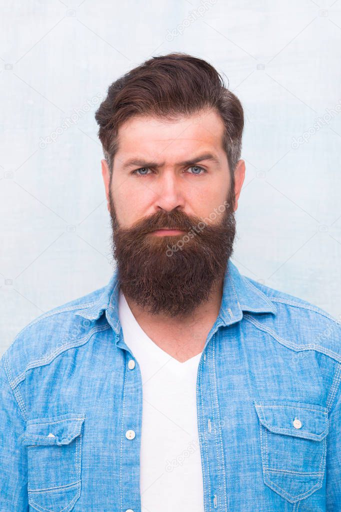 Well groomed macho. Hipster with beard and mustache wear denim shirt. Brutal handsome hipster man on grey wall background. Bearded man trendy hipster style. Masculinity and male beauty concept