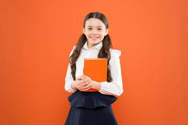 다시 학교에. 행복한 아이. 독서 수업. 서점 컨셉. 학교 유니폼을 입은 어린 소녀. 오렌지 배경에 메모를 작성하는 여학생. 정보 양식 북을 얻을 수 있습니다. 연구 와 교육. 교육 — 스톡 사진