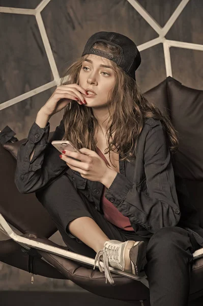 Красивая женщина в кепке в геометрическом кресле с сотовым телефоном — стоковое фото