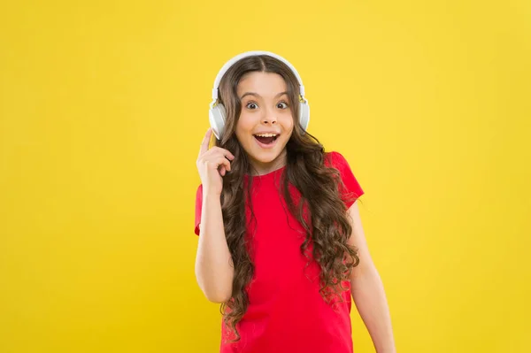 Teknologi adalah indah ketika bekerja. Gadis kecil yang bahagia mendengarkan musik menggunakan earphone dengan latar belakang kuning. Anak kecil menikmati teknologi suara stereo. Teknologi baru. Konsep teknologi — Stok Foto