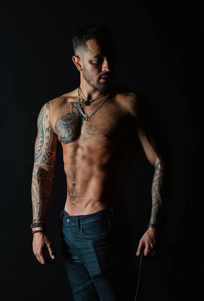 Modello di tatuaggio con pancia sexy. Uomo con braccio e petto tatuati. Uomo barbuto con busto forte. Sportivo o atleta in jeans moda. Cura del corpo con fitness e sport — Foto Stock