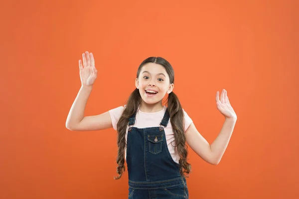 Ser glad och upphetsad. Lycklig liten flicka med söta leende på Orange bakgrund. Glatt litet barn glatt leende med mode look. Bedårande unge njuter lycklig barndom — Stockfoto