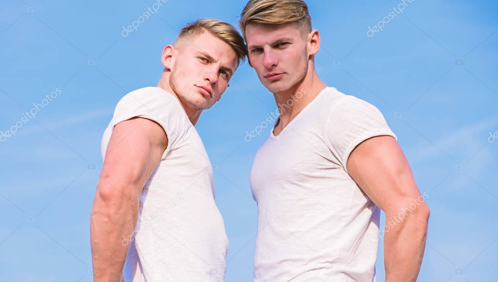 Men twins muscular brothers sky background. Handsome strong twins. Men strong muscular athlete bodybuilder posing confidently in white shirts. Attractive twins. Sport lifestyle and healthy body