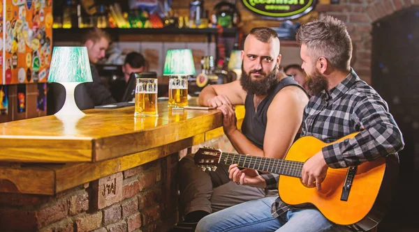 Man play guitar in bar. Cheerful friends relax with guitar music. Friday relaxation in bar. Friends relaxing in bar or pub. Real men leisure. Hipster brutal bearded spend leisure with friend in bar