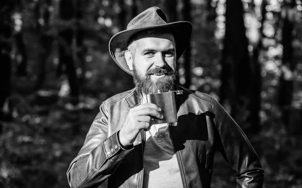 Country style. Bearded man in cowboy hat walk in park outdoor. man hipster relax in autumn forest. Spring weather. camping and hiking. mature male with brutal look drink alcohol from metallic flask
