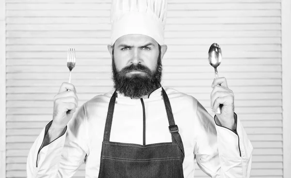 Es hora de probar. Chef cara seria mantenga cuchara y tenedor. Hombre guapo con barba sostiene utensilios de cocina sobre fondo blanco. Concepto de proceso de cocción. Vamos a probar el plato. Chef hambriento listo para probar comida —  Fotos de Stock