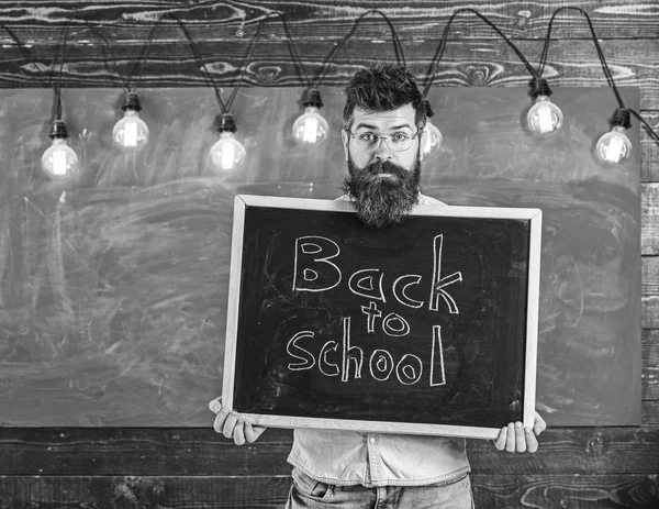 Enseignant sur visage surpris tient tableau noir avec titre de retour à l'école. Homme à la barbe accueille les étudiants, tableau sur fond. Le professeur jette un coup d'oeil hors du tableau. Concept de début d'année scolaire — Photo