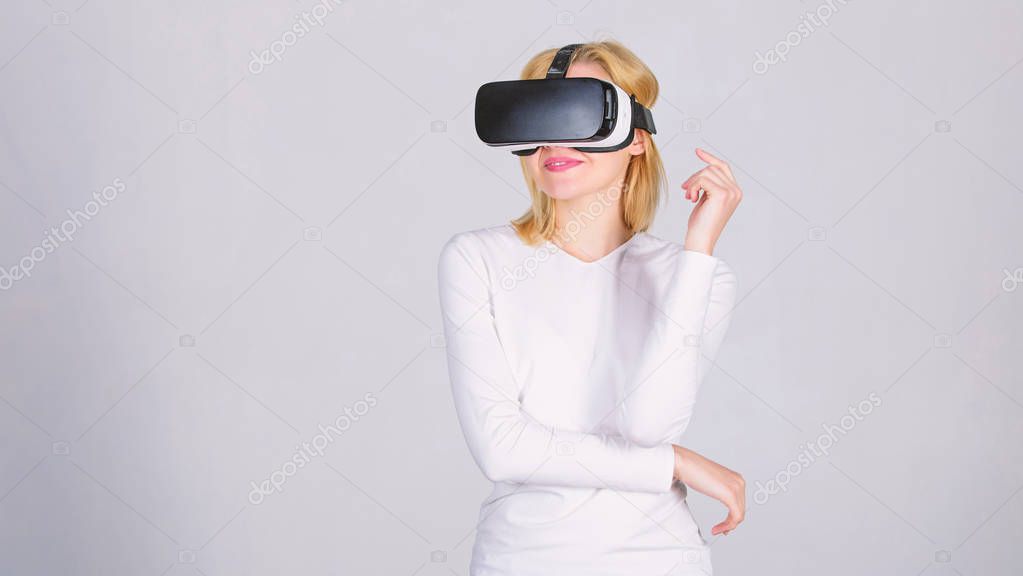 Amazed young woman touching the air during the VR experience. Portrait of an amazed girl using a virtual reality headset isolated on grey background. The woman with glasses of virtual reality.