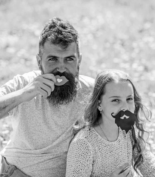 Padre posando con los labios y el niño posando con la barba foto cabina atributo. Concepto de roles de género. Familia pasar el ocio al aire libre. Papá e hija se sientan en la parcela de hierba, hierba en el backgrou — Foto de Stock