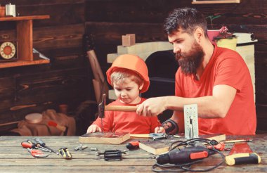 Babalık kavramı. Çocuk, çocuk ile baba çekiç kullanmayı öğrenme koruyucu kask içinde meşgul. Baba sakallı arka plan kara tahta çekiç, araçlarını kullanmak için küçük oğlu öğretim.