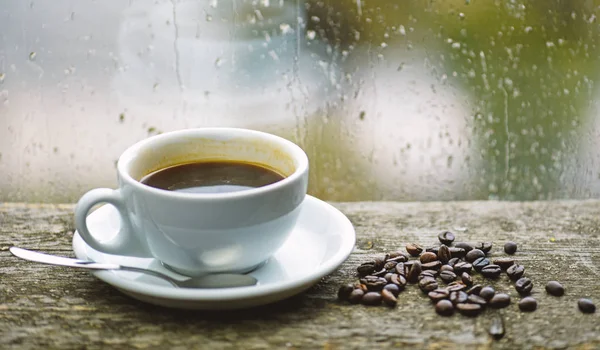 Autumn cloudy weather better with caffeine drink. Enjoying coffee on rainy day. Coffee morning ritual. Fresh brewed coffee white mug and beans on windowsill. Wet glass window and cup of hot coffee — Stock Photo, Image