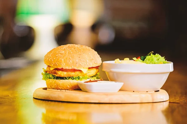 Snack alto en calorías. Hamburguesa y papas fritas y salsa de tomate sobre tabla de madera. Concepto de comida rápida. Hamburguesa con carne de queso y ensalada. Comida de engaño. Deliciosa hamburguesa con semillas de sésamo. Menú hamburguesa —  Fotos de Stock