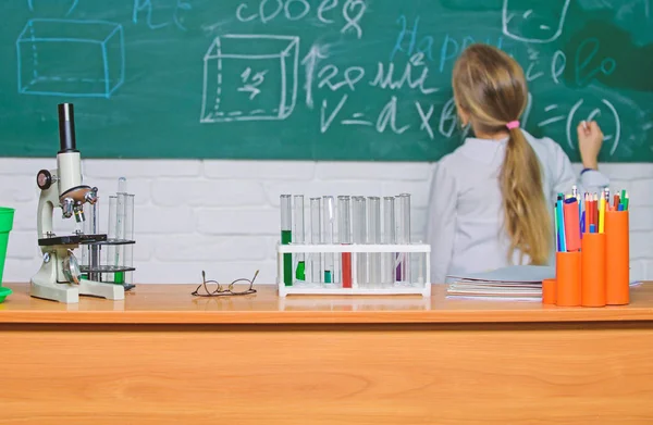 Ένα παιδί κοντά στο φόντο του σχολικού μαυροπίνακα. Μάθημα βιολογίας του σχολείου. Το παιδί μελετά τη βιολογία με εξοπλισμό στο σχολείο. Ημέρα της γνώσης. Η ιδέα της βιολογίας. Μικροσκόπιο και δοκιμαστικούς σωλήνες στο τραπέζι στην τάξη — Φωτογραφία Αρχείου
