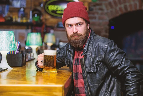 Bar is relaxing place to have drink and relax. Hipster relaxing at bar. Man with beard spend leisure in dark bar. Brutal lonely hipster. Friday evening. Brutal hipster bearded man sit at bar counter