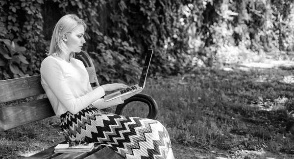 Woman with laptop works outdoor, green nature background. Freelance benefits. Lady freelancer working in park. Girl sit bench with notebook. Advantages and disadvantages of becoming freelancer