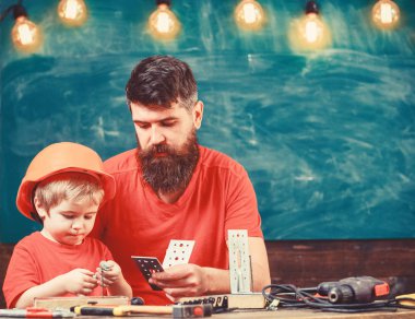 Evlat, Çocuk koruyucu kask içinde el ile onarım, babamla mı el sanatları yapar. Babası el ulağı kavram olarak. Baba, üst sakallı ve sınıfta, arka plan kara tahta küçük oğul