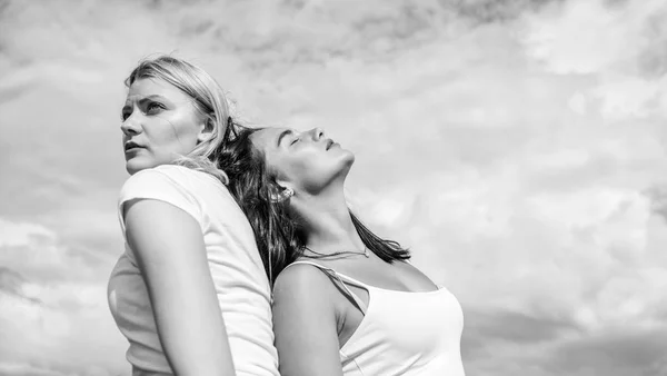 Alter ego concept. Blonde and brunette back to back. Concentrated and relaxed. Friend you trust. Friendship and trust. Female friendship. Women lean each other blue sky background copy space