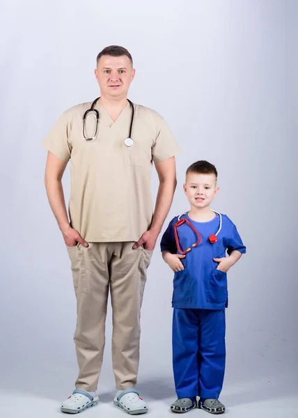 Father doctor with stethoscope and little son physician uniform. Future profession. Want to be doctor as dad. Cute kid play doctor game. Family doctor. Pediatrician concept. Medicine and health care