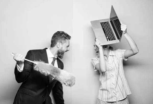 Getting onto a fight. Husband stand with dust brush while wife holding laptop. Couple of handsome man and pretty woman. Businessman and housewife. Family couple. Housekeeping or business