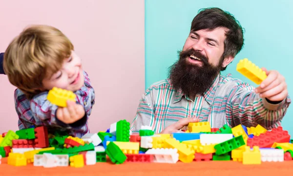 Dad and kid build plastic blocks. Child care development. Family leisure. Father son game. Father and son create constructions. Bearded man and son play together. Every dad and son must do together