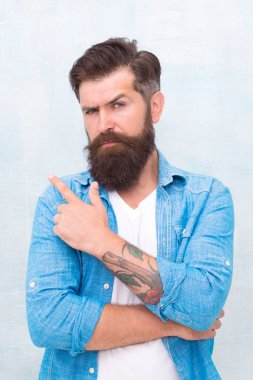 Berber salonu. Bakımlı maço. Gri duvar arka plan üzerinde Acımasız yakışıklı hipster adam. Sakallı adam moda hipster tarzı. Sakallı ve bıyıklı hipster denim gömlek giyer. Erkek güzellik konsepti