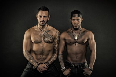 Machos with muscular tattooed torsos look attractive, dark background. Guys sportsmen with sexy muscular torsos. Athletes on confident faces with nude muscular chests. Sexy body concept clipart