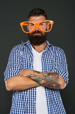 Gözlükler onun tarzı için mükemmel. Gri arka planda parti gözlüğü takan havalı bir adam. Acımasız hipster kollarını süslü gözlüklerle çapraz tutuyor. Moda gözlüklerinden bakan sakallı adam