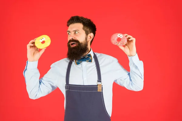 Inglasad donut. Skäggiga välvårdad man i förkläde sälja munkar. Donut mat. Bakade varor. Godis och kakor. Skräpmat. Hipster skäggiga Baker hålla munkar. Söt donut. Servitör i Café. Doughnut kalorier — Stockfoto