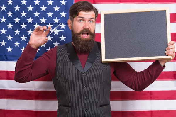 Hipster chique. Hipster barbudo segurando tesoura e quadro negro na classe. Homem Hipster no fundo da bandeira americana. Hipster barbeiro ensino barbeiro, espaço de cópia — Fotografia de Stock